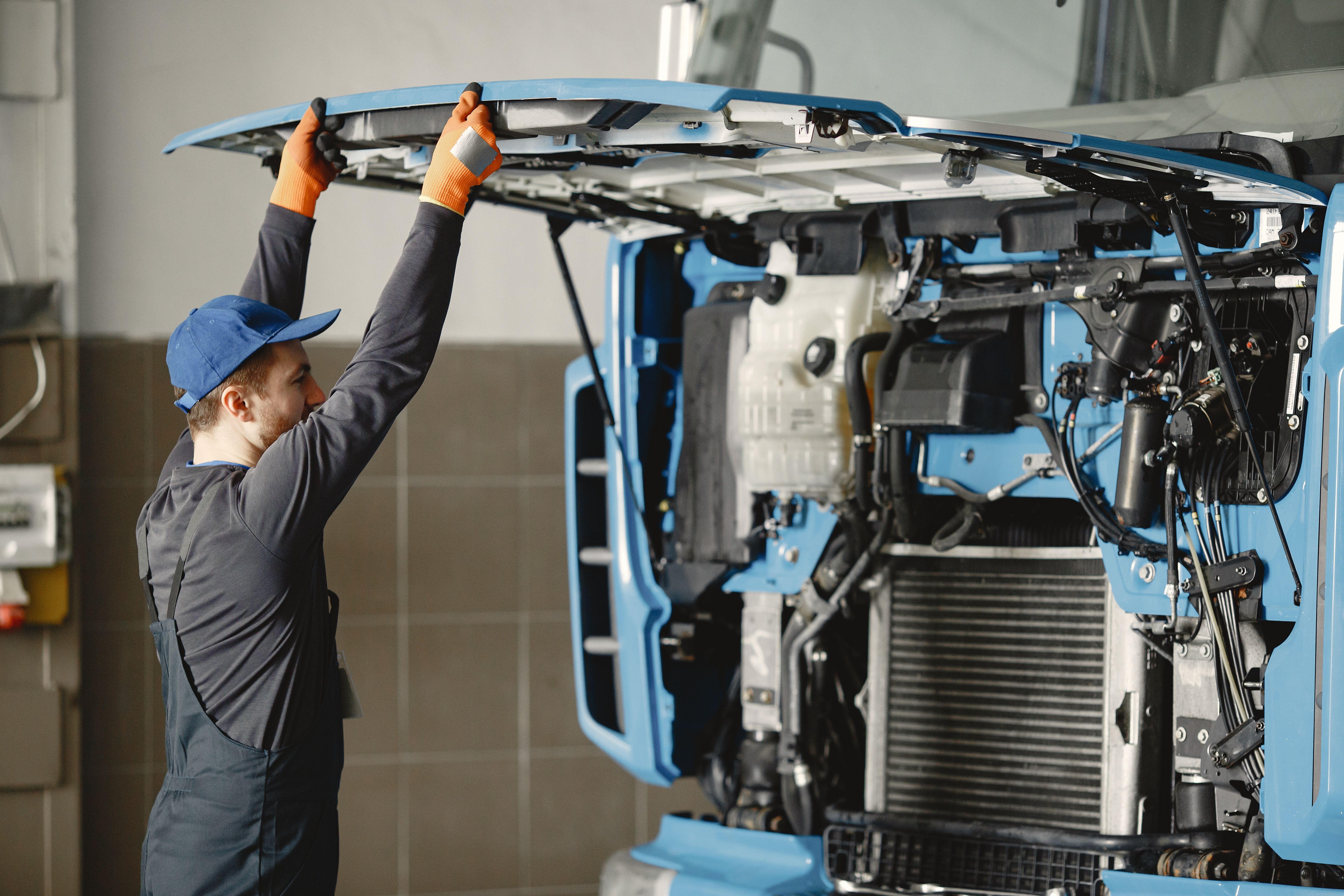 Technician lifting the front hood of a blue commercial truck to access the engine in a service shop
