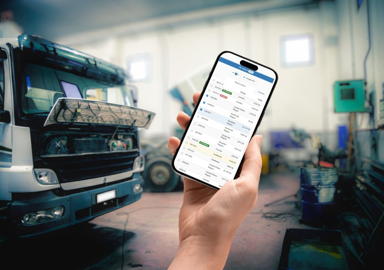 Hand holding a phone showing the Fleetrock mobile repair order list in a truck service shop