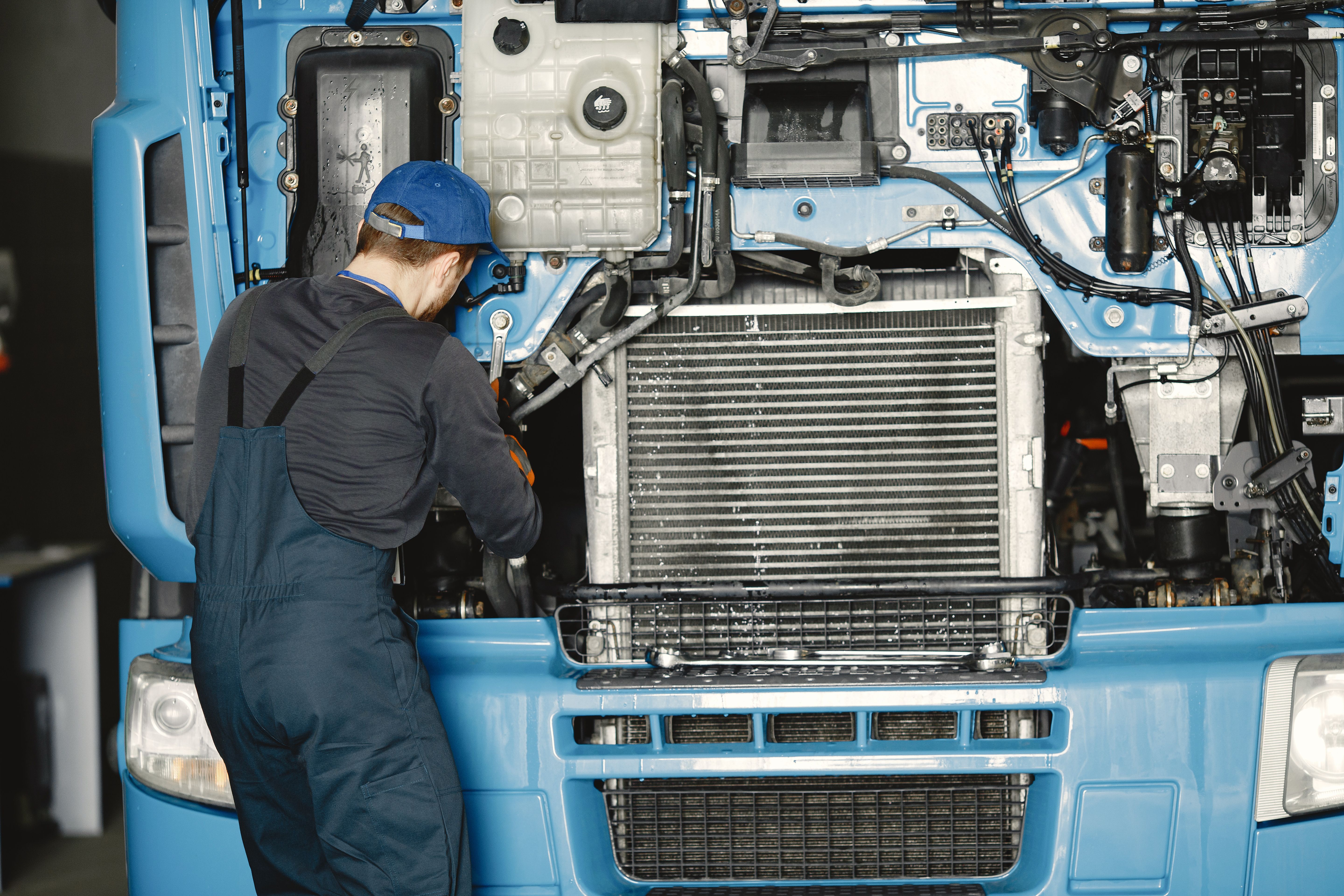 Technician servicing the front-end components of a blue commercial truck in a repair shop